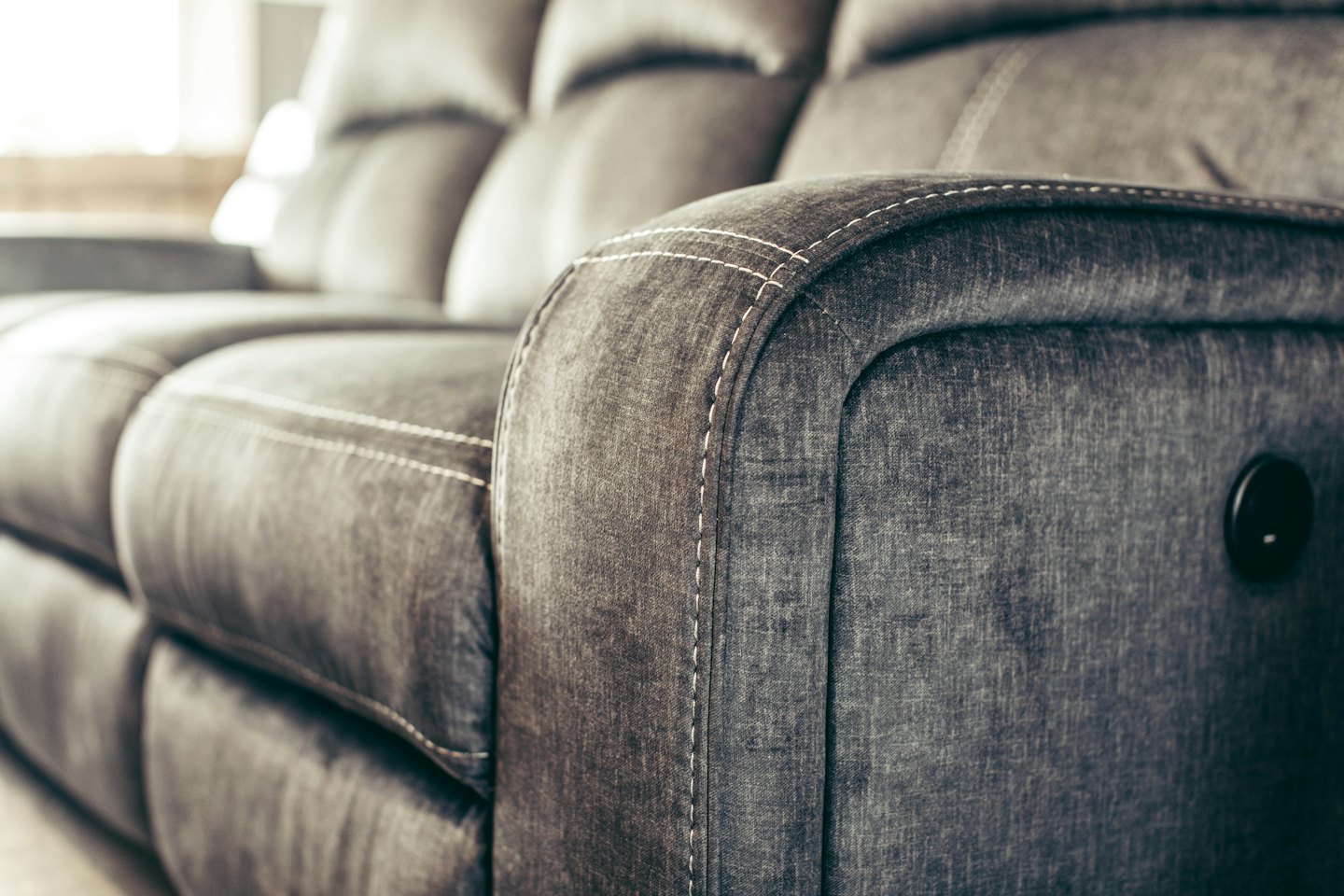 Modern grey fabric sofa with visible stitching and control.